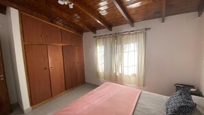A bedroom with a bed, wooden wardrobe, and a window with curtains.