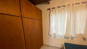 A room with a bed, a wooden wardrobe, and a window with curtains.