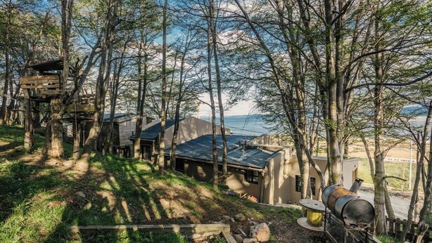 A cabin with a deck, a barbecue grill, and a view of the water.