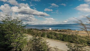 A road with trees and a distant view of a body of water and mountains.