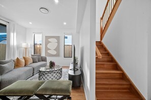 A modern living room with a grey sofa, a coffee table, and a staircase. - Luxury New Home| Prime Location|Easy City Access (Mount Gravatt East)