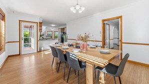Un comedor con mesa de madera, sillas y una cocina al fondo.