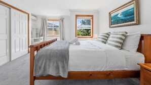 Un dormitorio con una cama, una ventana con cortinas, un cuadro y una mesita de noche de madera.