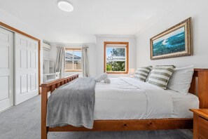 Een slaapkamer met een bed, een raam met gordijnen, een schilderij en een houten nachtkastje.