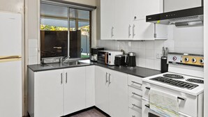 A modern kitchen with white cabinets, a black countertop, a stove, a coffee maker, and a window. - Affordable Stay | Private & Convenient |Near Shops (Jindalee)