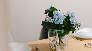 A dining table set with white plates, cutlery, and a vase with blue flowers. - Affordable Stay | Private & Convenient |Near Shops (Jindalee)