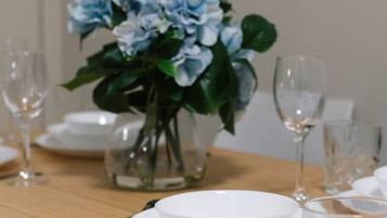 Een eettafel met witte borden, een helder glas en een vaas met blauwe bloemen.