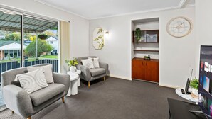 A modern living room with a grey sofa, a small white table, a wooden cabinet, and a large TV. - Affordable Stay | Private & Convenient |Near Shops (Jindalee)