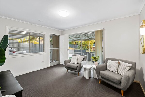 A modern living room with two grey sofas, a small white side table, and a large window with blinds.