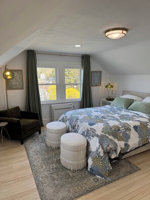 Ein Schlafzimmer mit einem großen Bett, zwei Nachttischen, einem Sessel, einem Fenster mit Vorhängen und einer Deckenleuchte.
