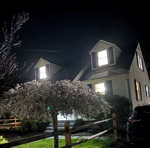 Ein zweistöckiges Haus mit einer sichtbaren Veranda und einem großen Baum davor.
