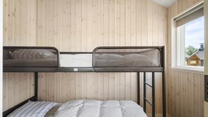 Ein Stockbett mit Moskitonetz-Kopfteil, ein Einzelbett darunter, Holzwandverkleidung und ein Fenster mit Blick auf ein Haus.