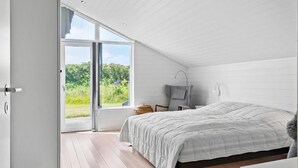 A bedroom with a large bed, a chair, a small table, and a view of greenery through a sliding door. - VillaVilla 954 - Fjaltring-Trans, Vestjylland (Lemvig)