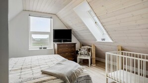 A bedroom with a sloped ceiling, a bed, a dresser, a television, a chair, and a crib. - VillaVilla 953 - Fjaltring-Trans, Vestjylland (Lemvig)