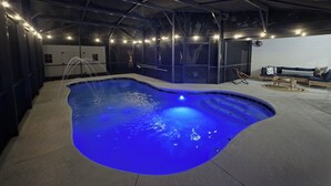 A swimming pool with a blue light, a lounge area with a sofa and chairs, and a white brick wall. - Pool Home + BBQ Grill + Family Friendly in Orlando, FL! (Orlando)