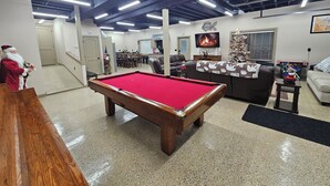 Une table de billard dans une pièce avec une cheminée, un sapin de Noël et un téléviseur.