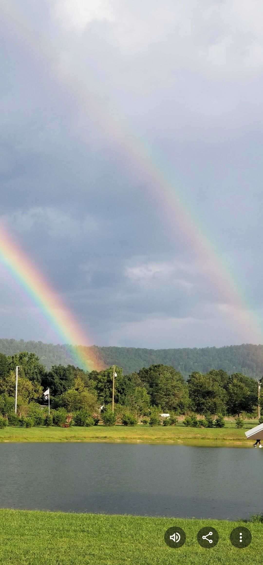 A landscape with a rainbow over a body of water, surrounded by greenery and trees.
