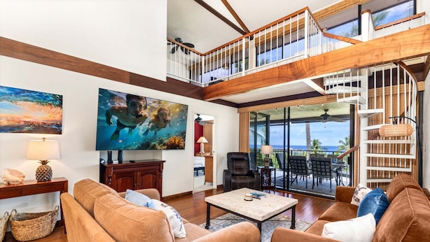 A spacious living area with a large painting, a sofa, a coffee table, and a view of the outdoors. - 🏖️Ocean View Condo w/ Loft + A/C in Bedrooms | Keauhou (Kailua Kona)