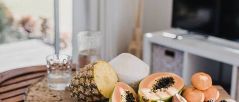 A wooden table with a variety of fruits and nuts, a glass of water, and pampas grass in the background.