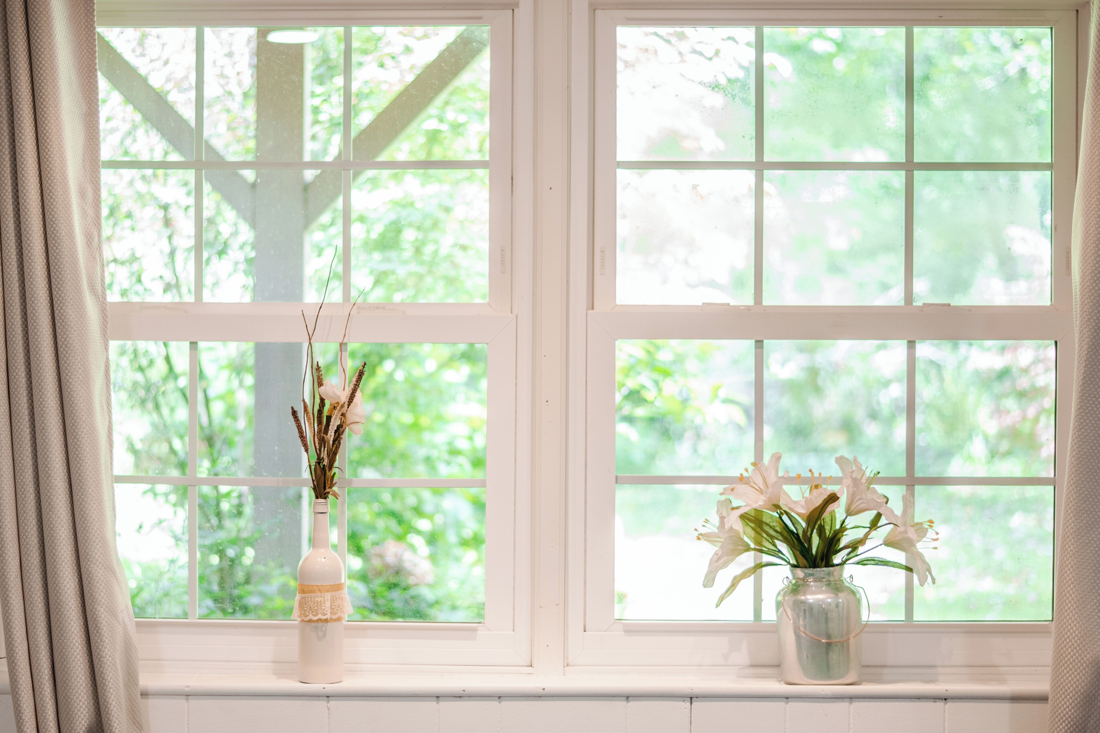 A window with two vases of flowers on a white window sill.