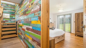 A bedroom with a colorful wooden wall, a bed, a wooden wardrobe, and a sliding glass door to the outside. - Seaesta Cottage, Holiday Cottage Broad Haven, Sleeps 8, 4 bedrooms,  bathrooms (Haverfordwest)