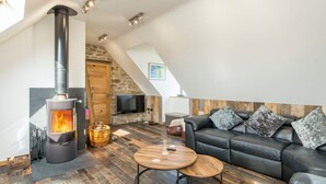 A modern living room with a wood-burning stove, a leather sofa, and a stone wall. - Seaesta Cottage, Holiday Cottage Broad Haven, Sleeps 8, 4 bedrooms,  bathrooms (Haverfordwest)