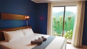 A hotel room with a bed, a view of greenery through the window, and a large window with curtains. - Windy's Leisure Villa  (Negombo)