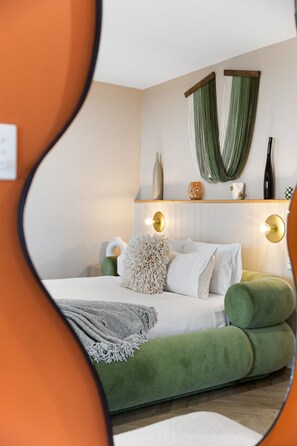 A bedroom with a bed, pillows, a green upholstered bench, a mirror, and a wall-mounted light fixture. - Sky Suite - A Panoramic Designer Studio in the Hills (Belair)