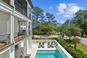 A modern building with a rooftop pool, outdoor seating, and a view of a tree-lined street. - New to VRBO, Steps to Beach, Pool, 5BR, Great Location (Hilton Head Island)