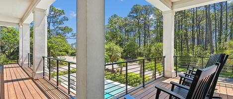 A covered outdoor area with wooden flooring, black metal railings, and a ceiling fan.