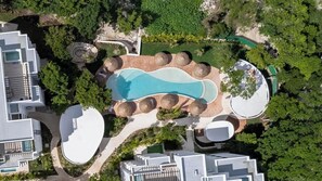 Luchtbeeld van een resort met een centraal zwembad, meerdere gebouwen en omliggend groen.