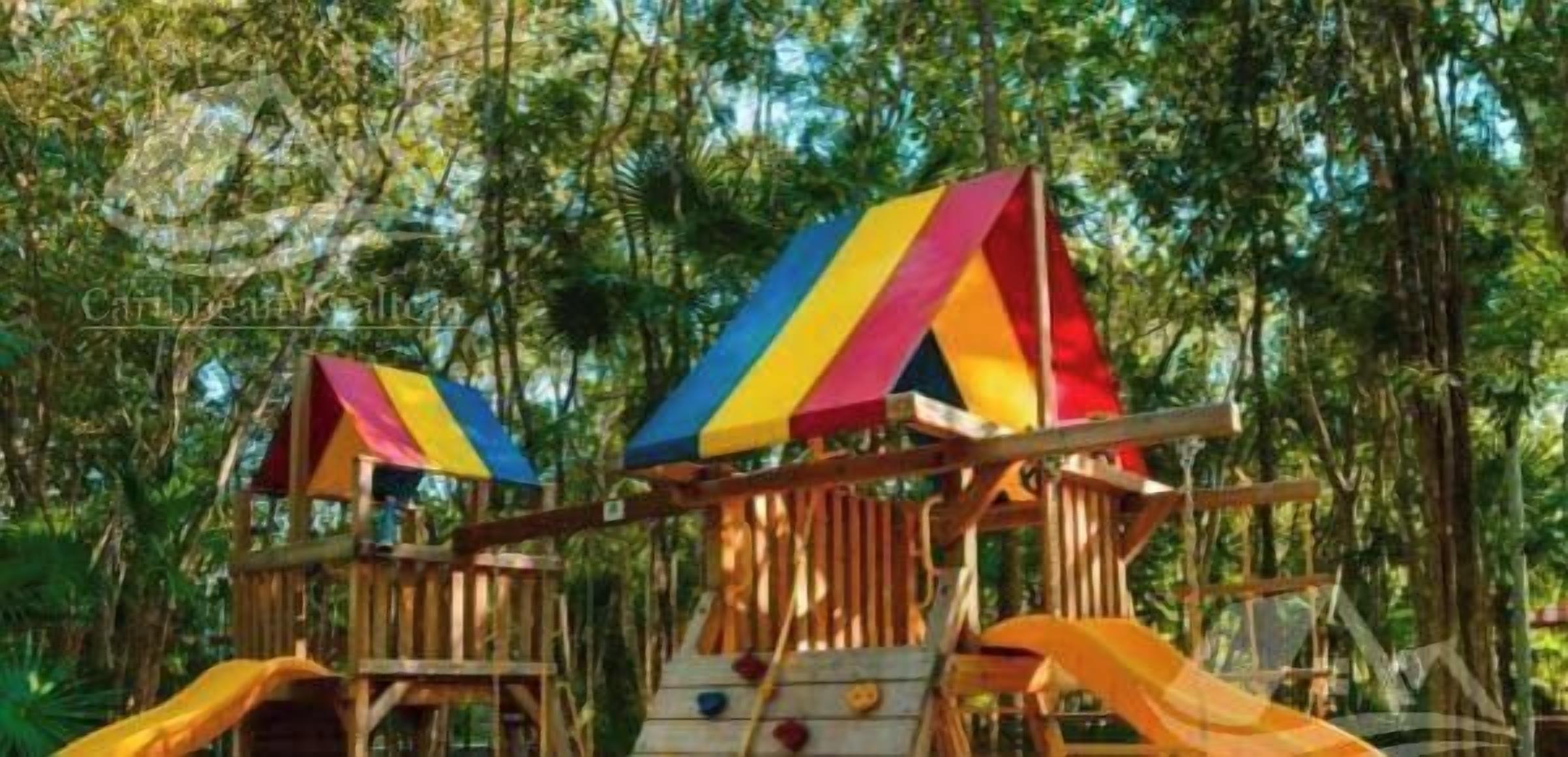 A wooden play structure with a slide and a climbing area, surrounded by trees.