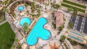 Eine Vogelperspektive zeigt ein Resort mit mehreren Schwimmbecken, einer sternförmigen Liegefläche und einem Parkplatz.