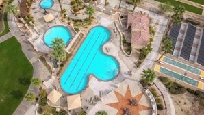 Vista aérea de un resort con varias piscinas, un patio solar en forma de estrella y un estacionamiento.