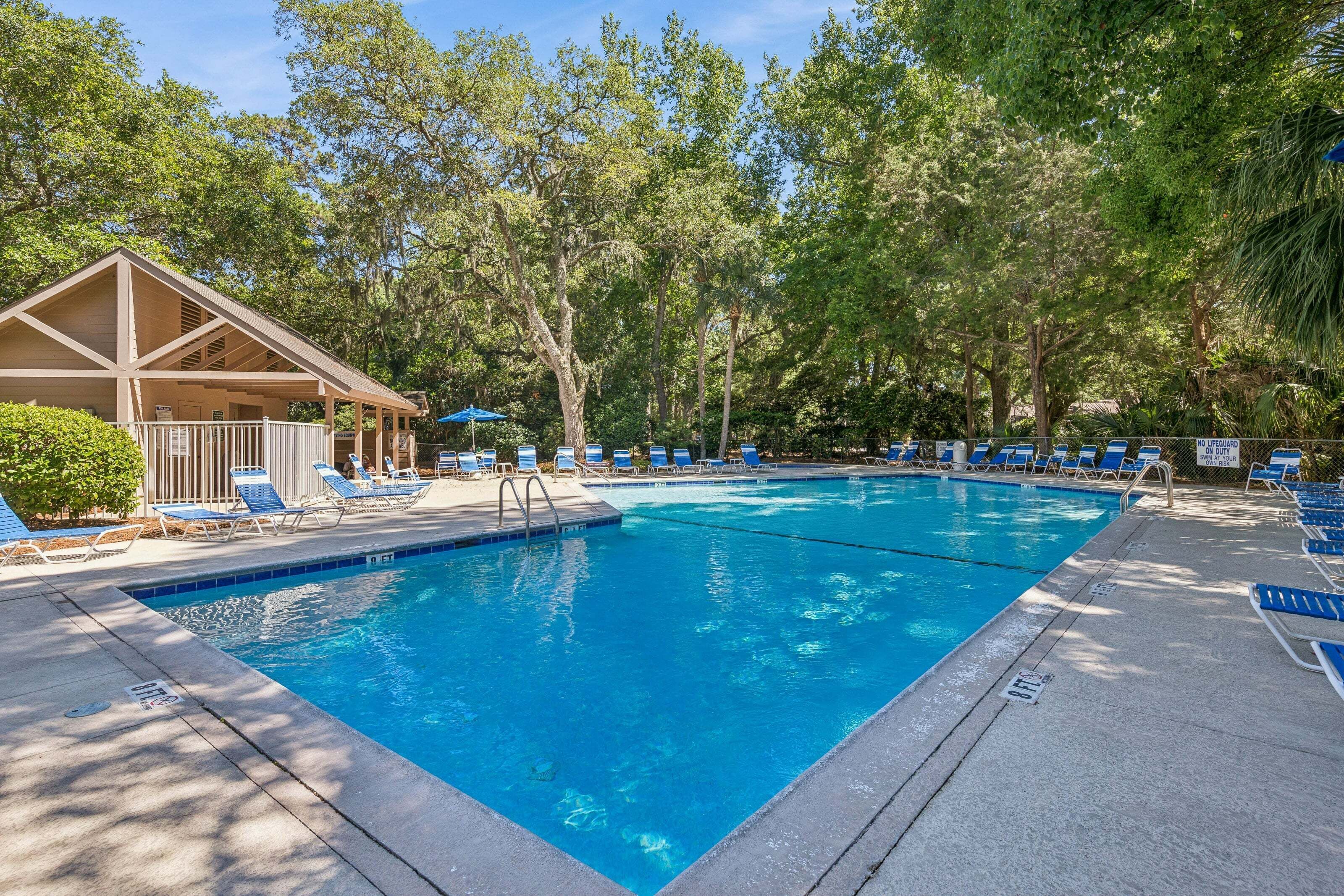A swimming pool with lounge chairs and a covered seating area surrounded by trees.