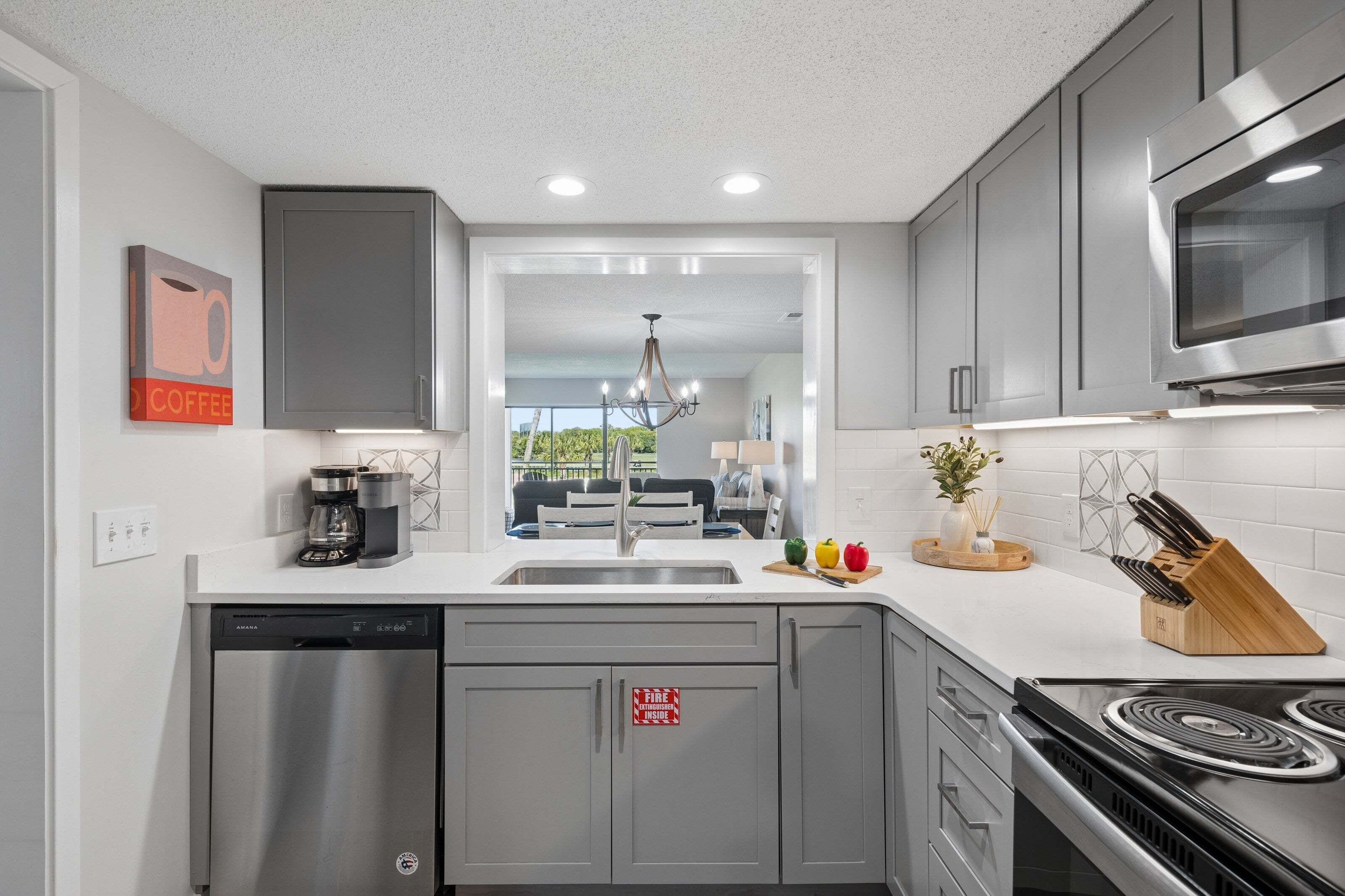 Una cocina moderna con gabinetes grises, lavavajillas de acero inoxidable, estufa y microondas.