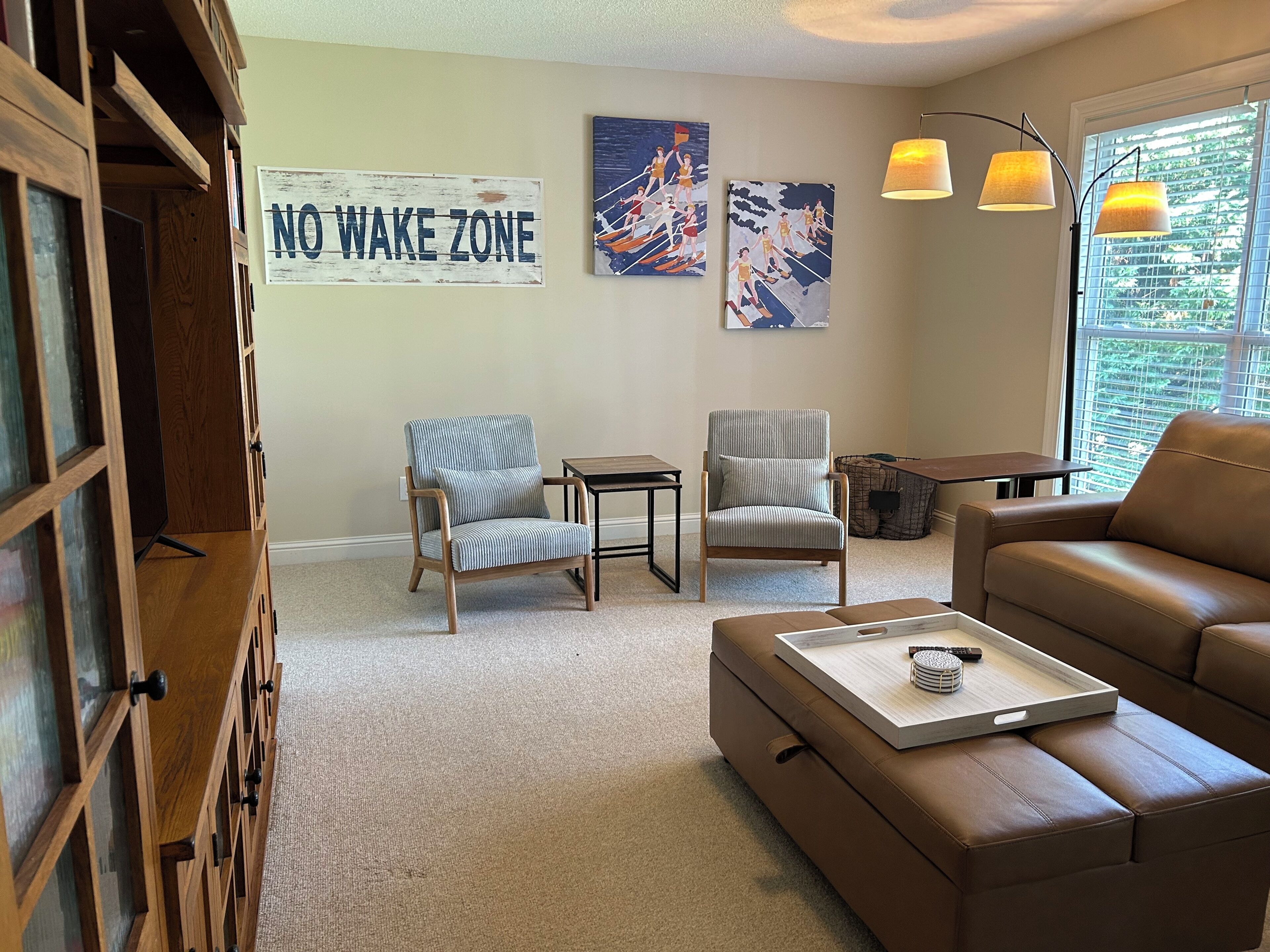 Uma sala de estar com um aviso de 'NO WAKE ZONE', dois poltronas, um sofá, uma mesa de centro e um abajur.