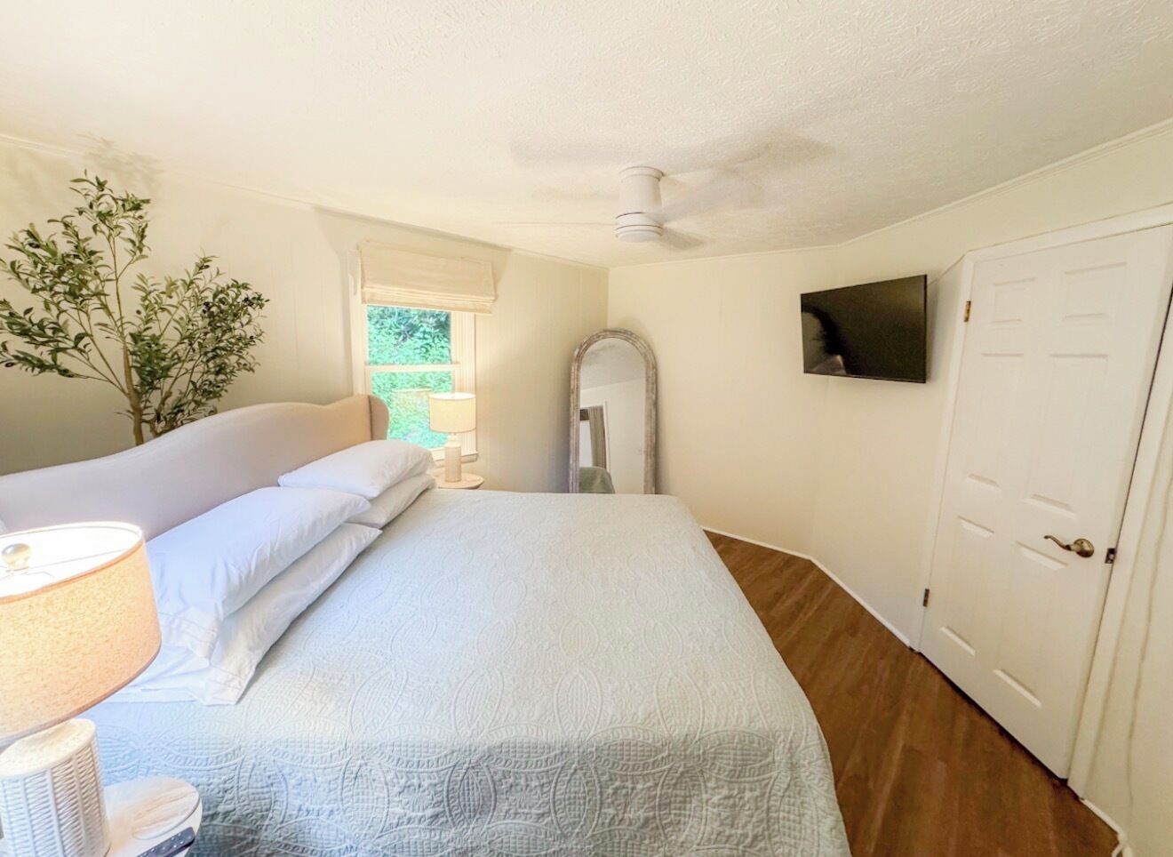 A bedroom with a bed, a bedside lamp, a mirror, a television, and a door.