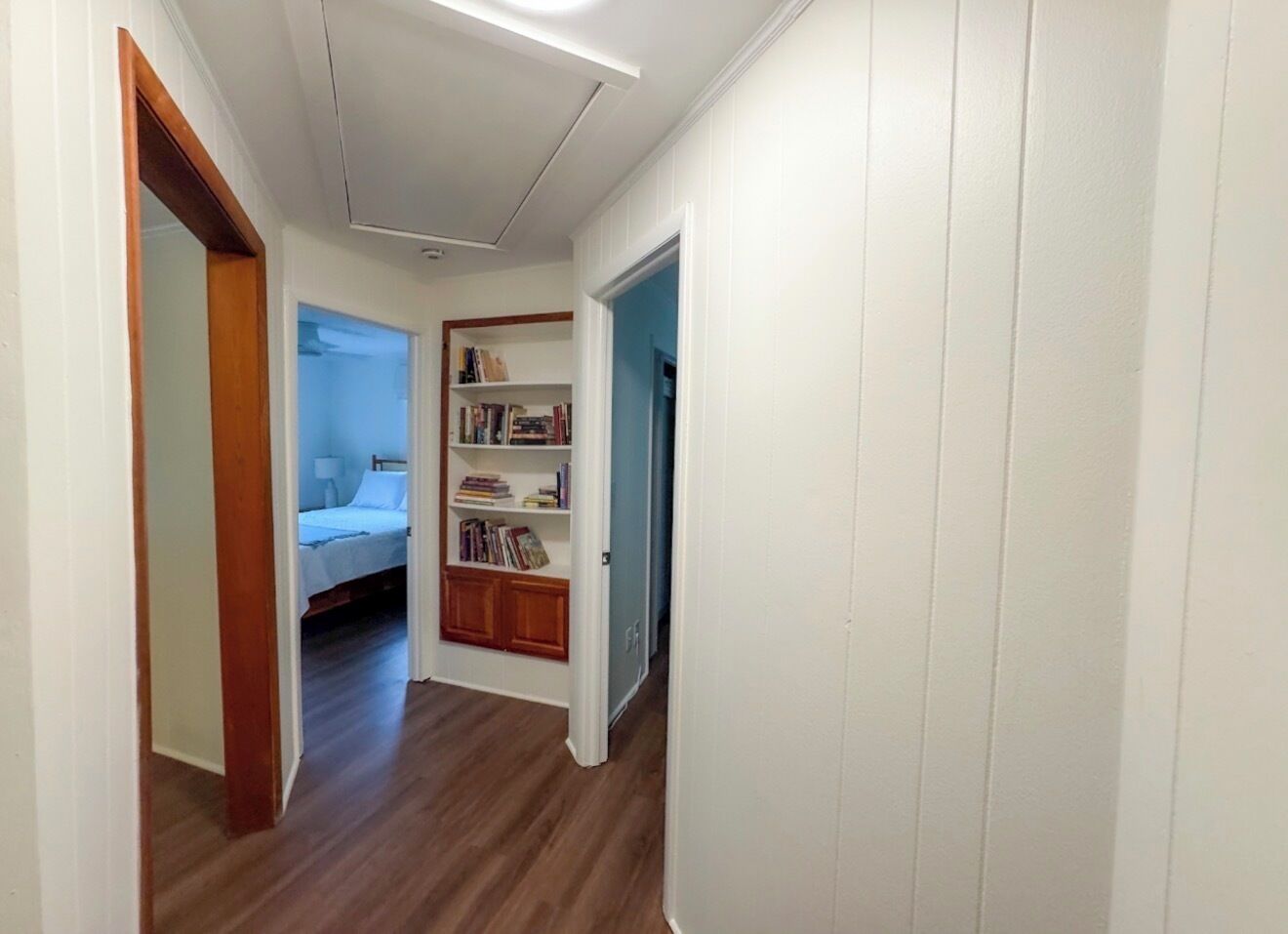 Un couloir avec un plancher en bois, un lit à l’arrière-plan et une bibliothèque remplie de livres.