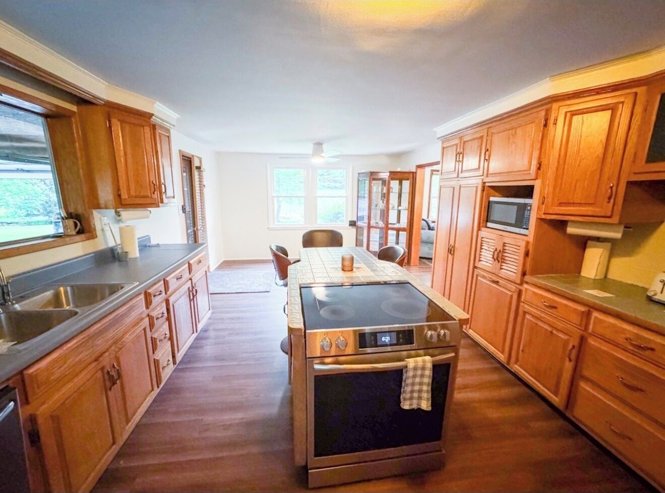 Una cocina con armarios de madera, una isla central con horno, una mesa de comedor con sillas y un ventanal grande.