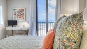Ein Schlafzimmer mit Bett, Schreibtisch, Computer und einem Fenster mit Blick auf den Strand.