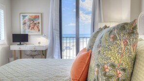 Ein Schlafzimmer mit Bett, Schreibtisch, Computer und einem Fenster mit Blick auf den Strand.