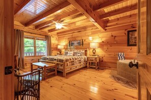 A wooden cabin interior with a bed, a desk, a chair, a window, a ceiling fan, and a fireplace. - S'more the Merrier - Mtn Views, Hot Tub + Game Loft (Sevierville)