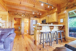 A wooden cabin interior with a kitchen, dining area, and a couch. - S'more the Merrier - Mtn Views, Hot Tub + Game Loft (Sevierville)