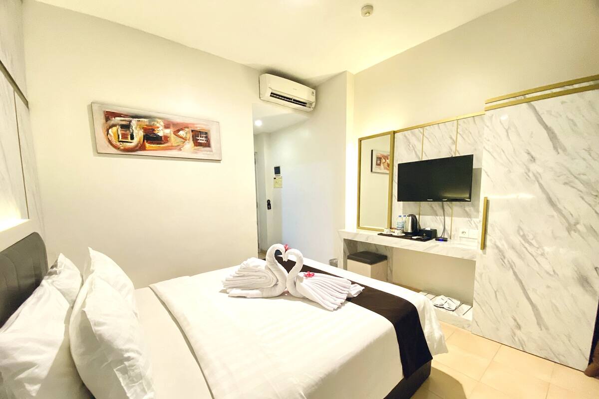 Ein Hotelzimmer mit Bett, Kissen, Fernseher, Spiegel und Klimaanlage.