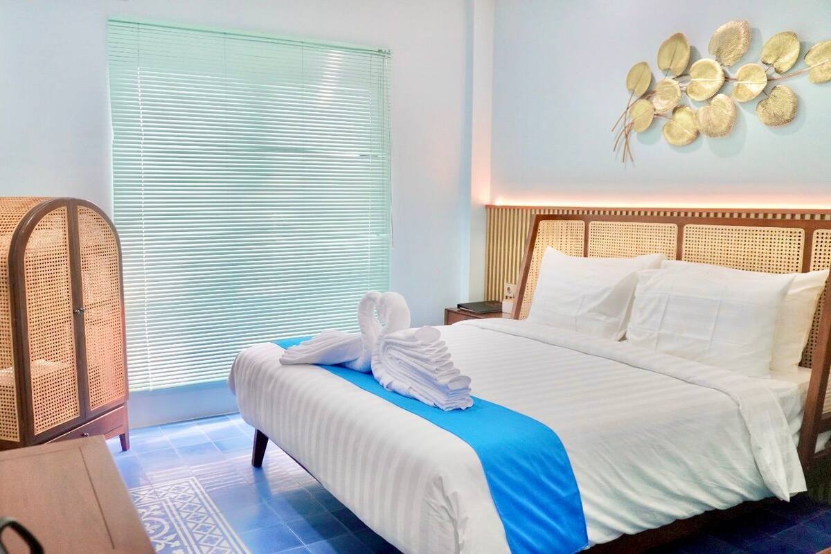 Ein Hotelzimmer mit einem Bett, einem Rattan-Sessel, einem Fernseher und einem Fenster mit Jalousien.
