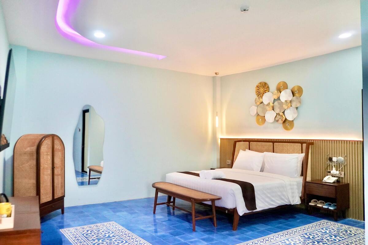 Ein Hotelzimmer mit Bett, Nachttisch, Spiegel und einem an der Wand befestigten Fernseher.