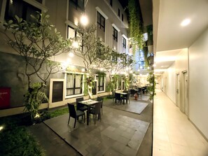 An outdoor dining area with tables and chairs, surrounded by plants and illuminated by string lights. - Grand Malioboro Hotel Yogyakarta (Yogyakarta)