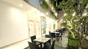 An outdoor dining area with tables and chairs, a small tree, and a wall with plants. - Grand Malioboro Hotel Yogyakarta (Yogyakarta)