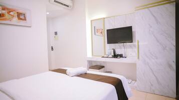A hotel room with a bed, a TV mounted on a marble wall, a small table with a coffee maker, and an air conditioning unit.